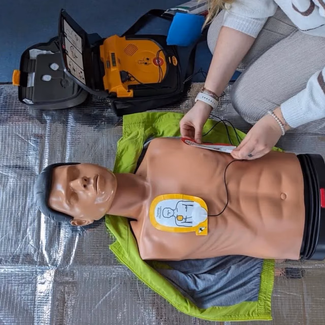 Übungs-Defibrillator mit aufgeklebten Elektroden auf dem Brustkorb einer Reanimationspuppe