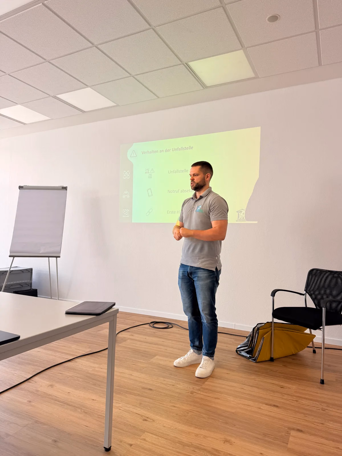 Ausbilder der Stadler Maidau Akademie steht vor Flipchart und Beamer-Projektion und erklärt einer Firmengruppe die Inhalte der Ersthelfer-Schulung