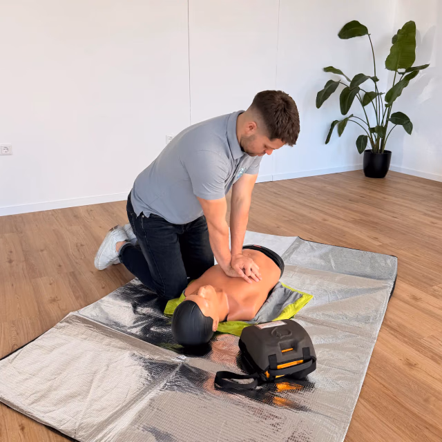 Kursteilnehmer kniet im hellen Schulungsraum neben einer Übungspuppe und führt die Herzdruckmassage durch